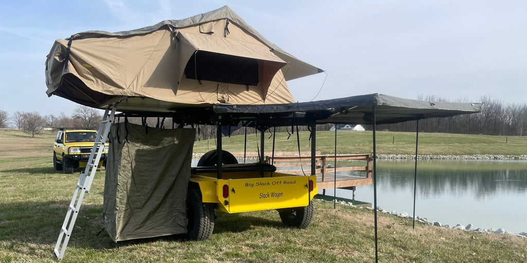 Yellow Slack Wagon set up for camping with rooftop tent, awning and shower tent by a pond