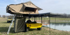 Yellow Slack Wagon set up for camping with rooftop tent, awning and shower tent by a pond